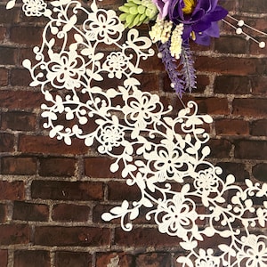 May include: White lace trim with a floral design against a brown brick background.