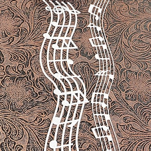 May include: White, die-cut musical notes and staff lines against a patterned background. The background features a floral design in shades of brown and black. A few artificial flowers are in the upper left corner.