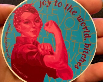 May include: A circular sticker featuring a red-toned illustration of a person flexing their arm, wearing a polka-dot headscarf. The background is teal with the repeating text VOTE and the red text joy to the world, bitches.