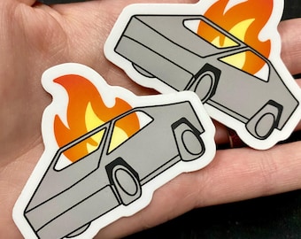 May include: Two die-cut stickers featuring a gray, angular, wedge-shaped car design with a bright orange and yellow flame graphic rising from the roof. The stickers have a white border and a smooth, matte-style finish on the surface.