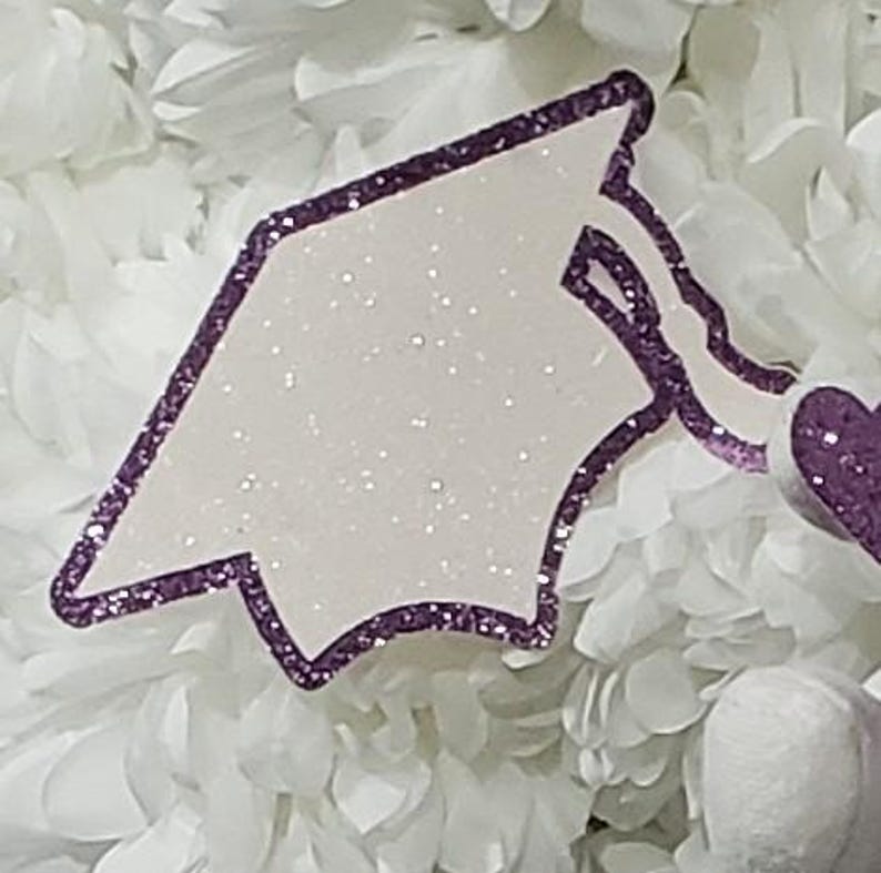 May include: A white graduation cap with a purple glitter border. The cap is on a white background.