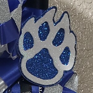 May include: A white paw print with blue glitter, a popular design for cheerleading accessories.