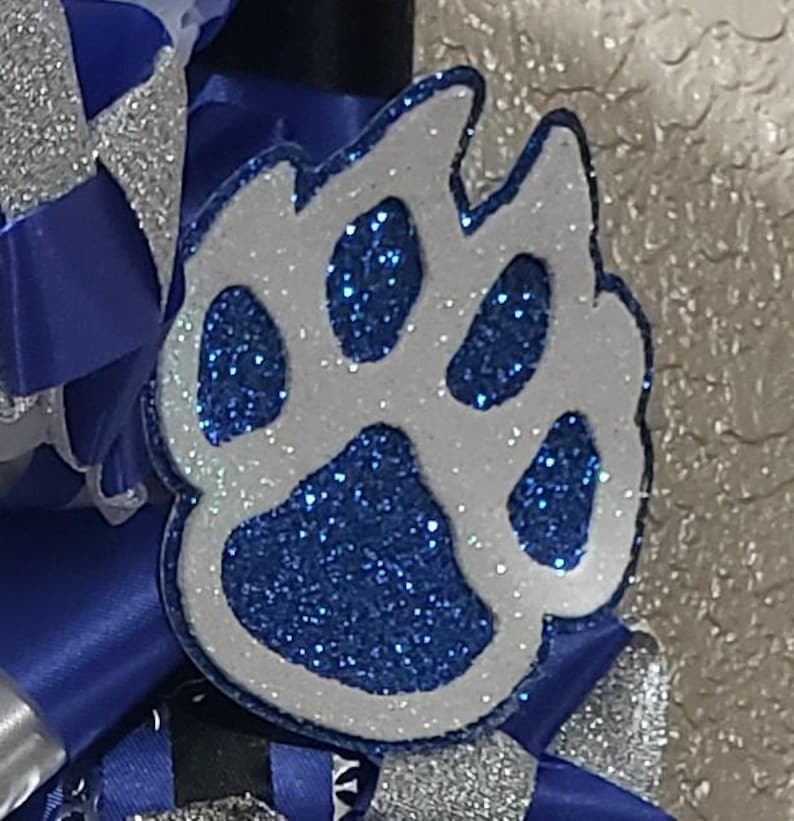 May include: A white paw print with blue glitter, a popular design for cheerleading accessories.
