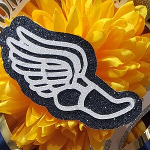 May include: A black and white glitter winged foot with a white outline. The foot is on a yellow flower.