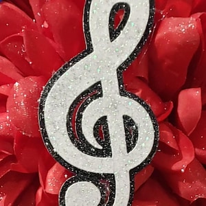 May include: A white glitter treble clef with a black outline on a red background.