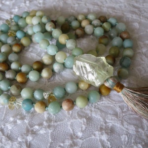 Puede incluir: Un collar de cuentas verdes y marrones con un colgante de cristal transparente y un borla. El collar est&aacute; hecho de piedras naturales y es perfecto para la meditaci&oacute;n o el yoga.
