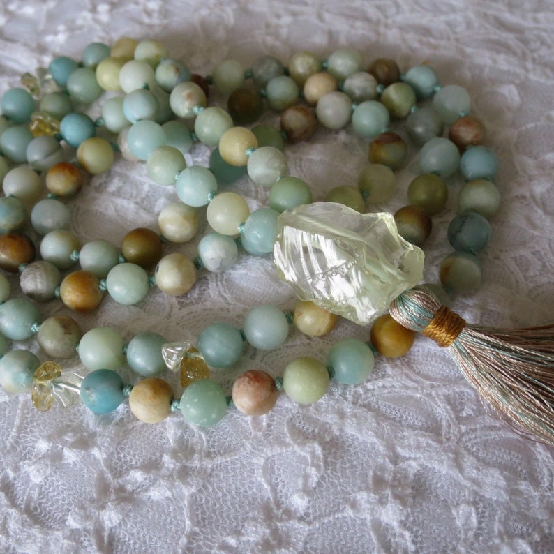 Puede incluir: Un collar de cuentas verdes y marrones con un colgante de cristal transparente y un borla. El collar est&aacute; hecho de piedras naturales y es perfecto para la meditaci&oacute;n o el yoga.