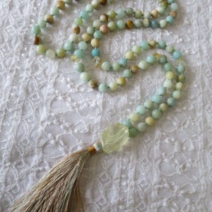 Puede incluir: Un collar mala verde y marr&oacute;n con un borla. El collar est&aacute; hecho de cuentas y tiene una piedra verde grande al final.