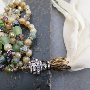 Op de afbeelding: Een meerstrengige ketting met groene, bruine en witte kralen, een met kristallen bezette hanger en een gouden kwast.