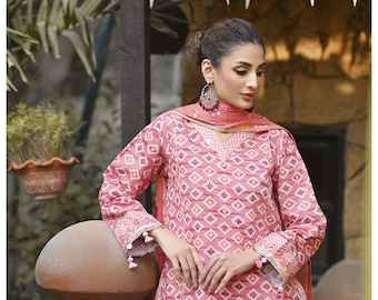 May include: A pink salwar kameez set with a geometric pattern. The long-sleeved top and matching scarf feature a repeating diamond design in shades of pink, white, and yellow. The outfit is worn with large earrings.