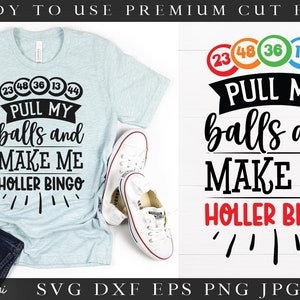 以下が含まれることがあります： 明るい青色のTシャツに、黒い文字で「Pull my balls and make me holler bingo」と書かれています。テキストの上に、数字の書かれたカラフルなビンゴボールが5つあります。Tシャツは白い表面に置かれ、白いスニーカーが2足あります。