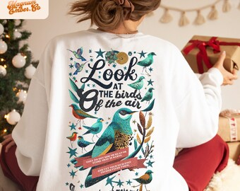 Puede incluir: Sudadera blanca con una ilustración de pájaro colorido y el texto "Mira las aves del cielo No siembran ni cosechan ni almacenan en graneros Y sin embargo, tu Padre celestial las alimenta ¿No vales tú mucho más? Mateo 6:26-27"