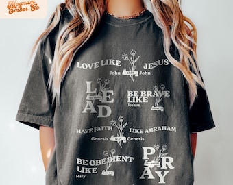 May include: A dark gray t-shirt with white text and floral designs. The text reads "LOVE LIKE JESUS John 13:34", "LEAD like Moses", "BE BRAVE LIKE Joshua", "HAVE FAITH Genesis 12:24", "LIKE ABRAHAM Genesis", "BE OBEDIENT LIKE Mary", and "PRAY like Hannah".