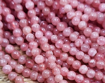 May include: A strand of pink gemstone beads. The beads are round and smooth, with a slightly translucent appearance. The beads are strung together on a clear thread.