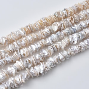 May include: Five parallel strands of irregular, flat, white and cream-colored shell beads. Each bead has a lustrous, pearlescent finish with a unique, organic shape. The beads are strung closely together, creating a textured, shimmering appearance.