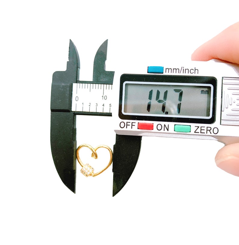 May include: A gold heart-shaped charm with a small cluster of clear rhinestones, measured at 14.7 mm using a digital caliper.