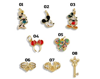 May include: A collection of gold-toned jewelry charms and rings featuring iconic cartoon characters. Includes a Minnie Mouse charm, Mickey Mouse charms, a bow headband, a Mickey Mouse head charm with colorful gems, and rings.