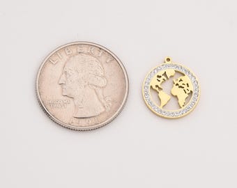 May include: A gold-colored pendant in the shape of a world map, surrounded by a ring of small, clear crystals. The pendant is next to a U.S. quarter coin for size comparison. The pendant has a small loop at the top for a chain.