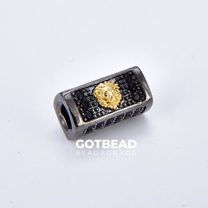K&ouml;nnte beinhalten: Schwarze und goldene Perle mit einem L&ouml;wenkopfdesign und schwarzen Akzenten. GOTBEAD BEAD FOR YOU ist unter der Perle aufgedruckt.