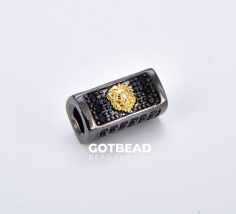 K&ouml;nnte beinhalten: Schwarze und goldene Perle mit einem L&ouml;wenkopfdesign und schwarzen Akzenten. GOTBEAD BEAD FOR YOU ist unter der Perle aufgedruckt.