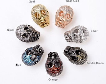 May include: Ten skull-shaped beads with different colored rhinestones. The beads are in the colors gold, rose gold, silver, black, blue, orange, and peridot green.
