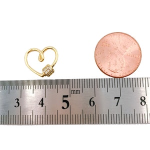 May include: A gold heart-shaped charm with a small cluster of clear cubic zirconia stones. The charm is approximately 5 millimeters in diameter and is shown next to a ruler for size reference.