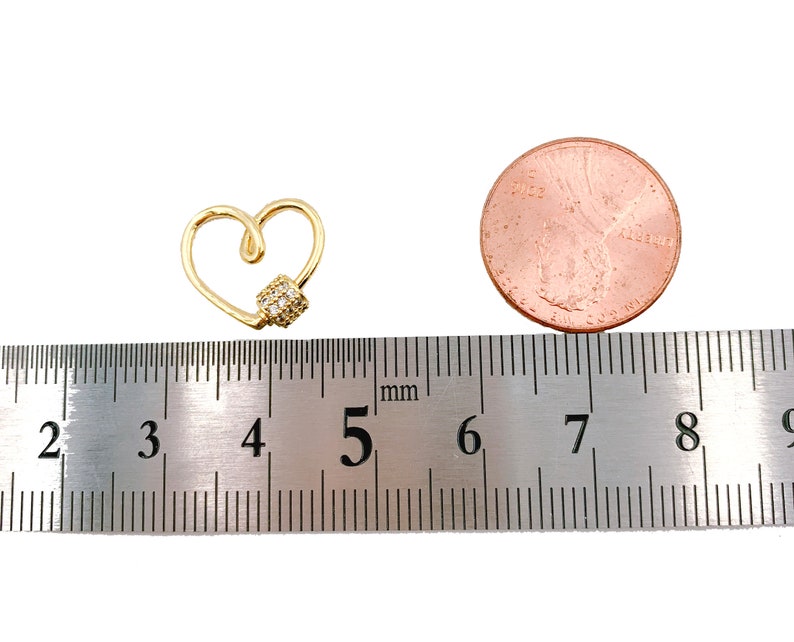May include: A gold heart-shaped charm with a small cluster of clear cubic zirconia stones. The charm is approximately 5 millimeters in diameter and is shown next to a ruler for size reference.