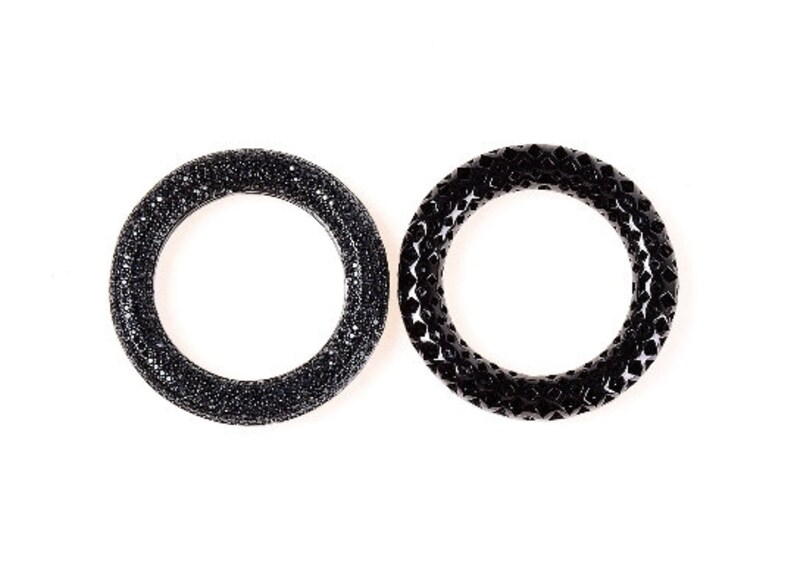 May include: Two black rings are displayed against a white background. The ring on the left is covered in small, sparkling black stones. The ring on the right has a geometric, textured design.