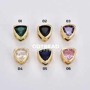 May include: Six gold-tone triangle-shaped charms with different colored gemstones. The charms are numbered 01 through 06.  The gemstones are green, black, purple, clear, blue, and pink.