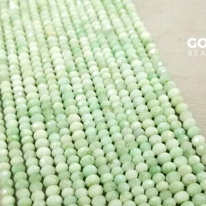 May include: A strand of light green faceted gemstone beads. The beads are small and round, and they are strung on a clear thread. The beads are arranged in a straight line, and they are all the same size and shape.