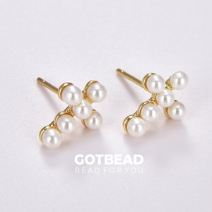 May include: A pair of gold earrings with a cross design made of small white pearls.