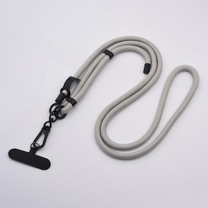 May include: A light grey phone lanyard with a black attachment. The lanyard is made of a thick, woven rope-like material. The black attachment includes a clip and a phone holder.