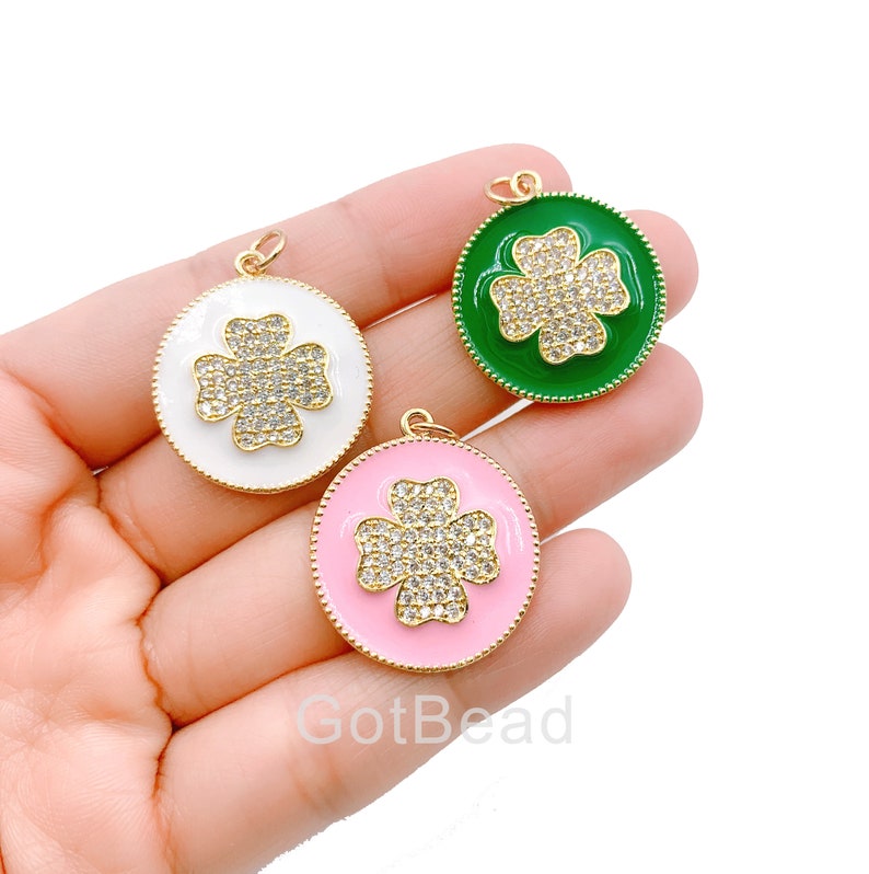 May include: Three gold-tone pendants with a four-leaf clover design. The clovers are encrusted with clear rhinestones and have a white, pink, and green enamel background.