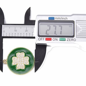May include: A close-up of a green enamel four-leaf clover charm with clear rhinestones. The charm is 2.7 cm in diameter and has a gold-tone finish.