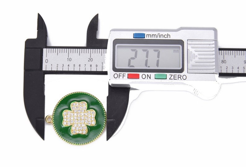 May include: A close-up of a green enamel four-leaf clover charm with clear rhinestones. The charm is 2.7 cm in diameter and has a gold-tone finish.