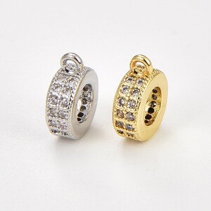 May include: Two round metal charms with a clear crystal design. One charm is silver and the other is gold.
