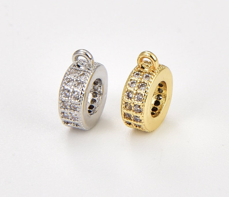 May include: Two round metal charms with a clear crystal design. One charm is silver and the other is gold.
