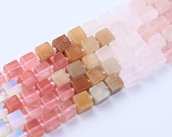 Peut inclure: Rangées de perles cubiques de différentes couleurs, notamment rose, pêche et beige. Les perles sont enfilées, créant un effet de dégradé. Les perles translucides semblent être en pierre polie ou en verre.