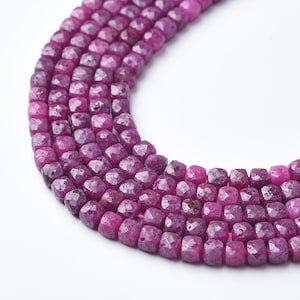 May include: Close-up of strands of faceted, deep magenta ruby beads. The beads are square-shaped and strung together, creating a textured, gemstone jewelry design. The beads are a rich, saturated color.