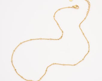 May include: A delicate gold-colored necklace with small, evenly spaced beads. The necklace has a simple design with a lobster clasp closure and an adjustable chain. The jewelry is displayed on a white background.