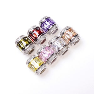 May include: Seven silver charm beads with different colored gemstones. The beads are round and have a silver band around the middle. The gemstones are purple, red, green, yellow, pink, clear, and orange.