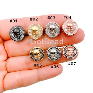 May include: Seven round beads with skull designs in various metallic finishes: black, gold, silver, and rose gold. Each bead has a skull design with surrounding embellishments. The text "GotBead" is visible.