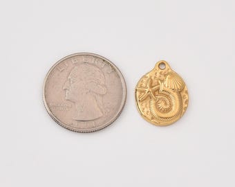 May include: A gold-colored pendant with a seashell, starfish, and spiral design. The pendant is next to a quarter coin for size comparison. The pendant has a small hole at the top for a chain.