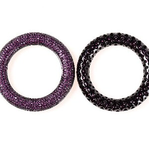 May include: Two circular bracelets. One is a deep purple, covered in small, sparkling crystals. The other is black with a textured surface and small purple crystals. Both are set against a white background.