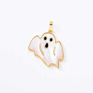 May include: A gold-toned pendant in the shape of a ghost. The ghost is white with a pearlescent sheen and a pinkish hue around the edges. It has two black eyes and a black mouth. The pendant has a gold bail.