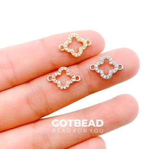May include: Three clover-shaped charms with clear rhinestones. The charms are gold, silver, and rose gold.
