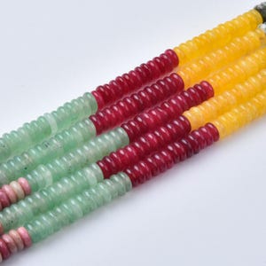 May include: Four parallel strands of small, disc-shaped beads arranged in a color-blocked pattern. Each strand features segments of light green, deep red, and bright yellow beads, with small pink beads visible at the bottom of the strands.