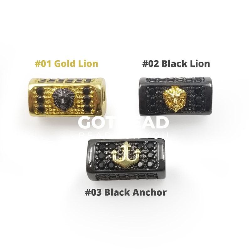 K&ouml;nnte beinhalten: Drei rechteckige Gl&uuml;cksbringer-Perlen in Gold und Schwarz mit unterschiedlichen Designs. Die erste Perle zeigt einen goldenen L&ouml;wenkopf mit schwarzen Zirkonia-Steinen. Die zweite Perle zeigt einen schwarzen L&ouml;wenkopf mit schwarzen Zirkonia-Steinen. Die dritte Perle zeigt einen goldenen Anker mit schwarzen Zirkonia-Steinen.