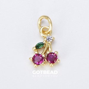Op de afbeelding: Gouden bedel met twee rode kersen en groene bladeren, versierd met heldere strass steentjes. De bedel heeft een lus om aan een ketting of armband te bevestigen.