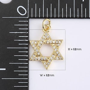 May include: Gold-colored Star of David pendant, 12mm wide and 12mm high, encrusted with small, clear crystals. The pendant has a loop at the top for attaching to a chain or bracelet. The Star of David is a symbol of Judaism.